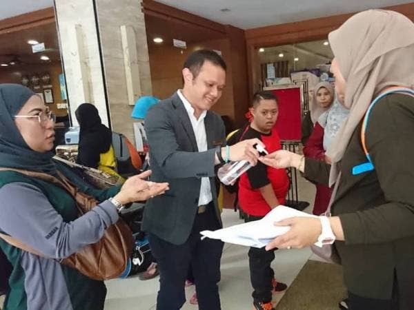 Seow Chee Han (tengah) memberikan cecair pembunuh kuman kepada pelanggannya di pekarangan lobi resortnya di Bukit Katil hari ini.