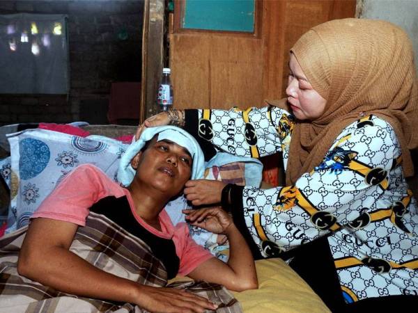 Pengerusi Sahabat Charity Balqish, Rukiza Abu Bakar (kanan) membantu menguruskan pesakit kanser kulit tahap empat, Syarifah Syarimah ketika ditemui di rumahnya di Kampung Kolon. Foto: Bernama