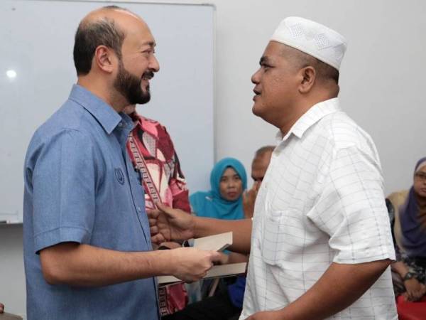 Mukhriz (kiri) menyerahkan sumbangan bantuan kepada penerima yang layak di Pusat Khidmat Dun Jitra hari ini.