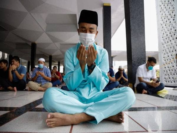 Seorang lelaki lengkap memakai topeng muka mengaminkan bacaan doa sebelum menunaikan solat Jumaat di Masjid Negara hari ini. - Foto Bernama