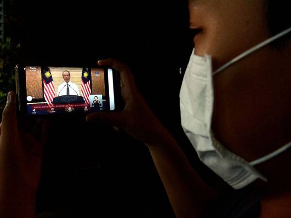 Seorang penduduk Kampung Peramu mengikuti pengumuman rasmi oleh Perdana Menteri, Tan Sri Muhyiddin Yassin berhubung langkah-langkah kerajaan berkaitan penularan Covid-19 yang disiarkan secara langsung menerusi telefon pintarnya. -Foto Bernama