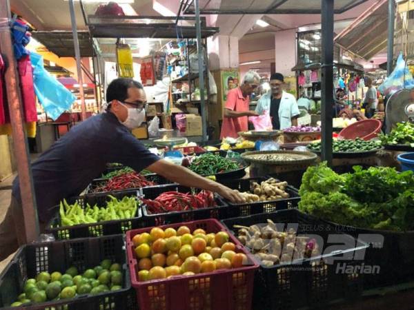 Hassan (kanan) melayan pelanggan yang berkurangan pada hari pertama Perintah Kawalan Pergerakan dikuatkuasakan.