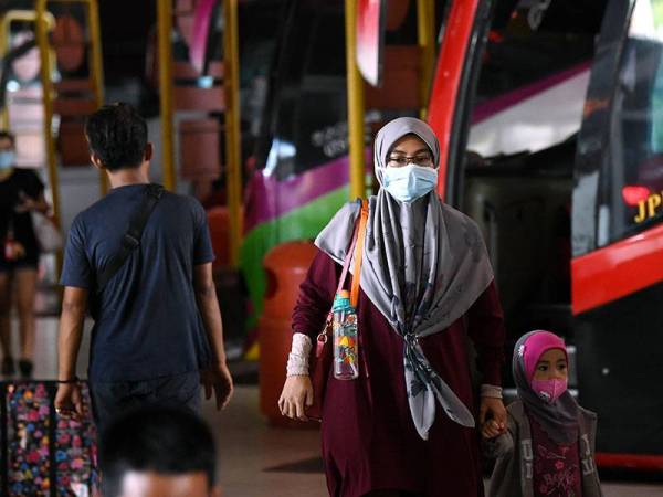 Sepasang ibu dan anak menggunakan penutup hidung dan mulut ketika menunggu bas. - Foto Bernama