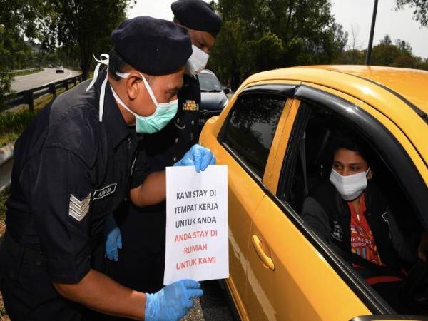 Seorang anggota polis menunjukkan sekeping kertas yang tertulis “Kami Stay Di Tempat Kerja Untuk Anda, Anda Stay Di Rumah Untuk Kami” semasa membuat pemeriksaan kenderaan berikutan tempoh Perintah Kawalan Pergerakan bermula 18 Mac hingga 31 Mac ini di Jalan Tun Dr Awang di sini hari ini.- Foto Bernama