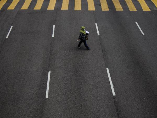 Seorang wanita dilihat melintasi jalan ketika tinjauan mengenai Perintah Kawalan Pergerakan hari ketiga terhadap rakyat di negara ini. -Foto Bernama
