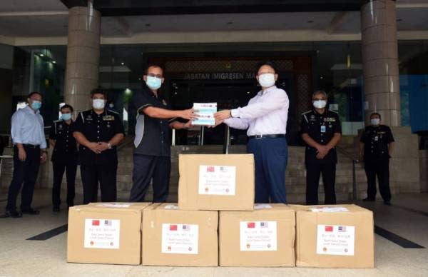 Khairul Dzaimee (kiri) menerima sumbangan daripada Bai Tian berupa 10,000 topeng muka di Ibu Pejabat Imigresen Putrajaya hari ini.