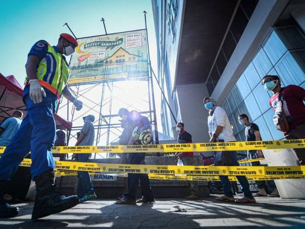 Anggota keselamatan melintas barisan orang ramai yang beratur untuk membeli barang keperluan di Pasar Raja Bot ketika tinjauan Perintah Kawalan Pergerakan (PKP) di sekitar Jalan Chow Kit hari ini. - Foto Bernama