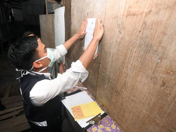 Kakitangan Jabatan Kesihatan menampal notis penutupan sebuah kedai yang masih beroperasi di luar waktu dibenarkan sewaktu operasi COVID-19 bersama polis di Kampung Forest malam tadi. - Foto Bernama