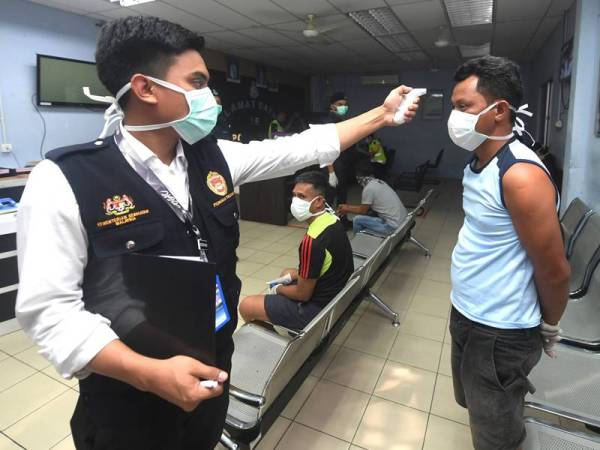 Kakitangan Jabatan Kesihatan memeriksa suhu badan seorang penduduk yang ditangkap kerana ingkar arahan sewaktu operasi COVID-19 di Balai Polis Sandakan malam tadi. - Foto Bernama
