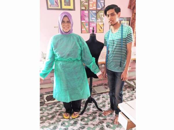Pemaju Masyarakat Jahitan Kemas Sepang, Safuan Salleh (kanan) menunjukkan baju makmal pakai buang untuk kegunaan petugas perubatan yang dijahit Sukarelawan Kemas.
