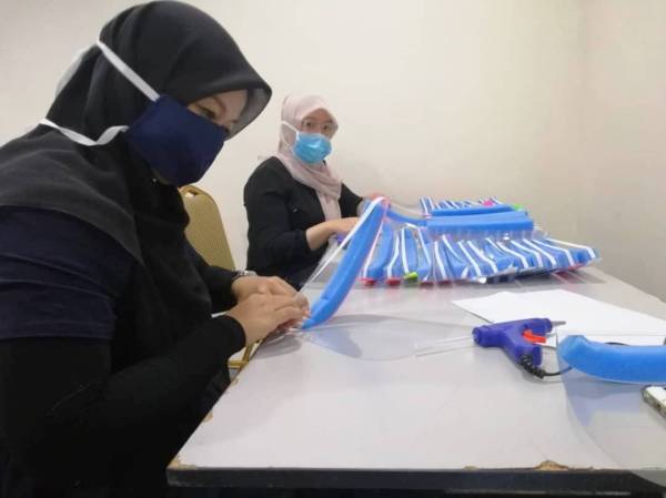 Sukarelawan sedang memotong span untuk ditampal di atas pelindung muka yang dihasilkan secara DIY.