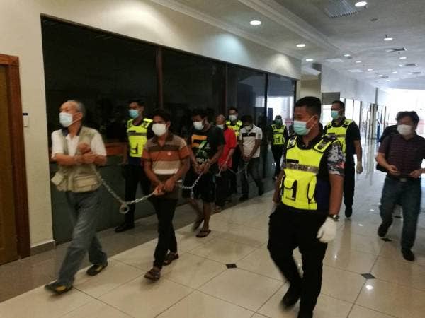 Lelaki warga Jepun (depan) bersama 10 yang lain diiringi anggota polis ketika dibawa ke Mahkamah Majistret di sini hari ini untuk sebutan kes langgar PKP.