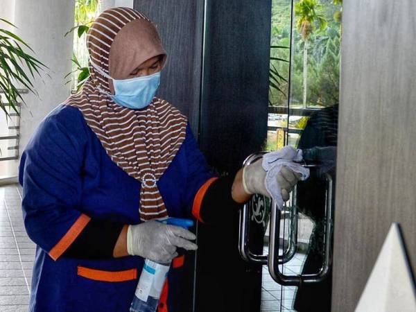 Seorang kerja pembersihan UPSB sedang membersihkan pintu di sebuah bangunan di UUM bagi memastikan kawasan kampus bebas wabak Covid-19.