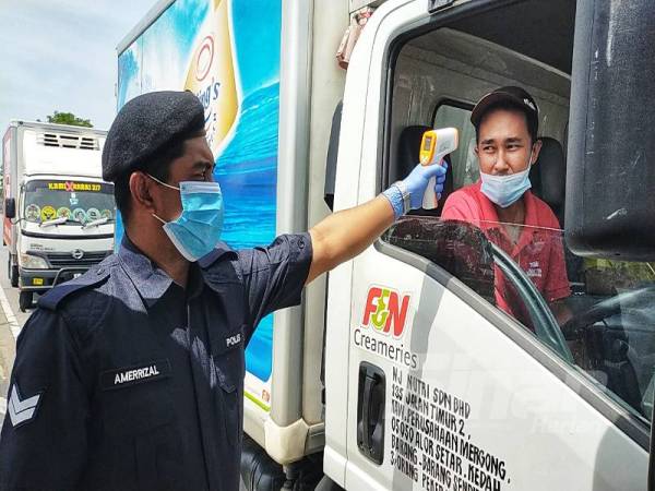 Seorang anggota sedang memeriksa suhu pemandu lori yang melalui sekatan jalan raya di Kepala Batas hari ini. 