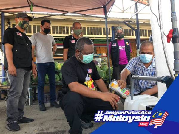 Wan Zuhari membantu Ahmad Deraman memasukan cecair antiseptik ke dalam tong berisi air. 