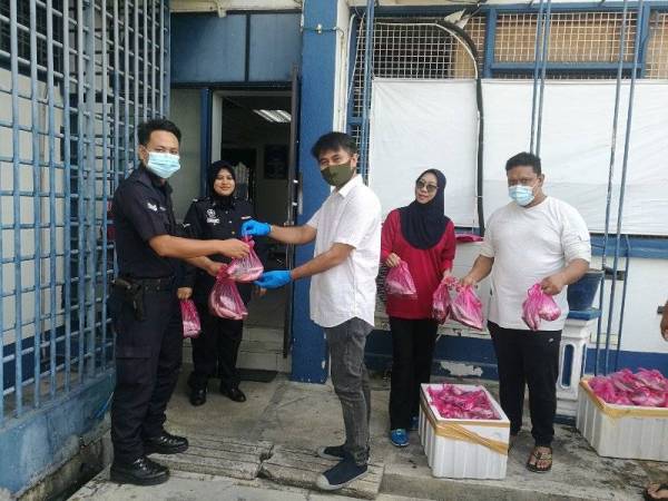 Norali (kanan) menyerahkan bungkusan ikan kepada anggota Balai Polis Sungai Senam sebagai tanda penghargaan kepada pasukan keselamatan yang bertungkus lumus ketika tempoh PKP.