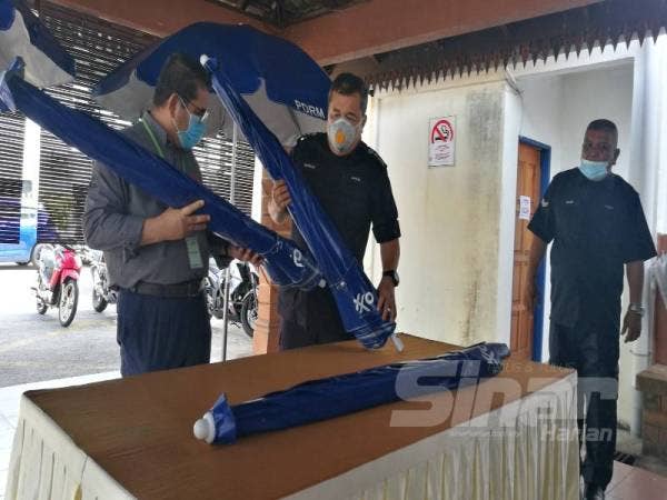 Wakil ExxonMobile, Mohd Badli Mohd Ali (kiri) menyerahkan payung kepada Roslee untuk kegunaan anggota di sekatan jalan raya (SJR) sepanjang PKP.