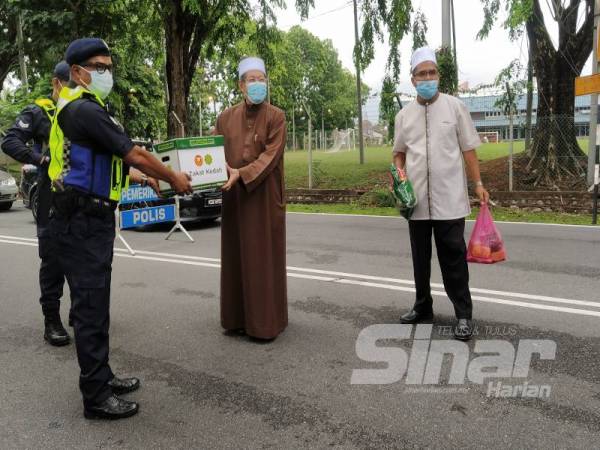 Fadzil (tengah) menyerahkan sumbangan kepada petugas sambil diperhatikan Syeikh Zakaria (kanan) di Pos Kawalan Polis Taman Rakyat Mergong di sini hari ini.