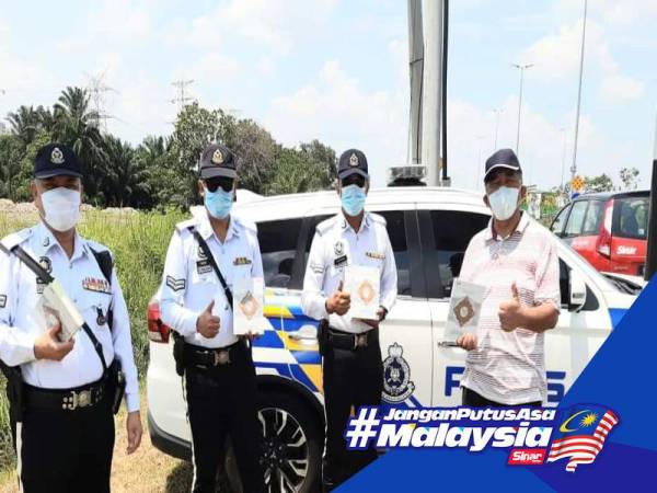 Sekretariat Projek Wakaf Al-Quran merangkap Pengurus Kanan Tugas-Tugas Khas Kumpulan Karangkraf Sdn Bhd, Hashim Anang (kanan) menyerahkan infak al-Quran kepada petugas keselamatan di sekatan jalan raya di Jalan Kebun Baru Batu 9 Kuala Langat petang tadi.