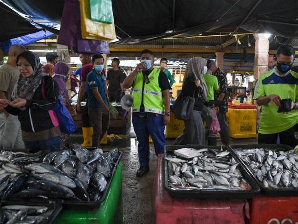 Penguatkuasa Majlis Bandaraya Kuala Terengganu (MBKT) Nurul Al-Hafez Mat Dagang (tengah) menggunakan pembesar suara bagi memastikan orang ramai yang mengekalkan penjarakan sosial sebagai langkah membendung penularan COVID-19 ketika membeli barangan basah di Pasar Borong Gong Pauh hari ini. - Foto Bernama