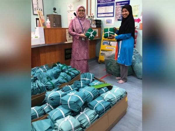 Siti Salina Samaun (kanan) menyerahkan sumbangan PPE yang sudah siap dijahit kepada Wan Nur Amalina di Hospital Port Dickson semalam.