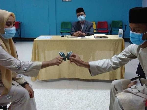 Aidilakmal (kanan) menyerahkan mas kahwin kepada Norafiqa dan disaksikan Mohd Nazri di Mini Auditorium Masjid Al-Azim, di Bukit Palah, di sini, hari ini.