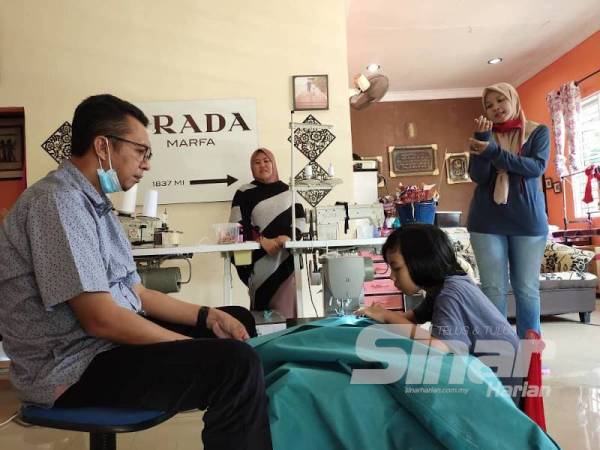 Saiful Yazan melihat adik Nur Afia Qistina menjahit PPE di rumahnya di Kampung Kepis Hilir, Johol.