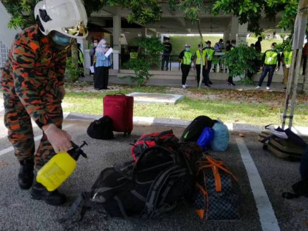 Anggota bomba melakukan proses sanitasi pada beg pelajar USAS yang dibenarkan pulang hari ini.