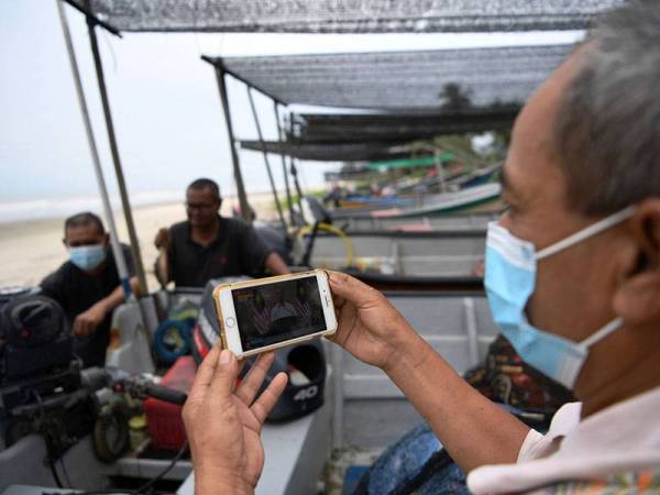 Nelayan Kampung Beserah Md Nor Osman, 55, (kanan) menonton perutusan khas Perdana Menteri Tan Sri Muhyiddin Yassin sempena Hari Pekerja hari ini.