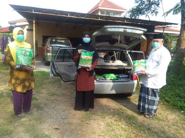 Cikgu Azmi (kanan) mengedarkan bantuan makanan keperluan kepada penduduk Kampung Pondok Batu Hampar, Merbok Kedah.