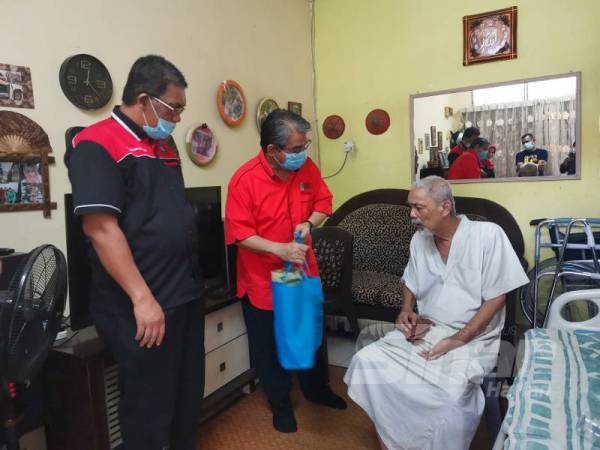 Supyan menyampaikan sumbangan barangan keperluan kepada Amran sambil diperhatikan Baharudin (kiri).