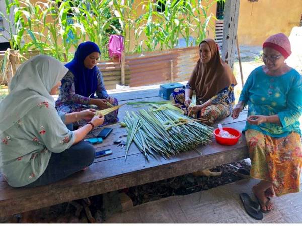 Rohimah (kiri) turut dibantu jirannya Esah Mamat, 66, (kanan) untuk kerja-kerja membentuk kelongsong ketupat daripada daun palas yang diperolehi dari hutan semak di hujung Kampung Kubang Palas, Banggu, Kota Bharu.