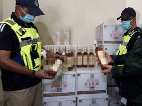 Muhammad (kiri) menunjukkan minuman keras berjenama yang dirampas di sebuah rumah dijadikan stor penyimpanan barang seludup di Bandar Baru Permas Jaya, Johor Bahru, hari ini.