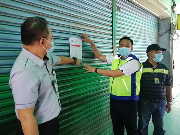 Mohd Rashidi (tengah) menampal notis penutupan sebuah restoran di Seksyen 19, Shah Alam hari ini.