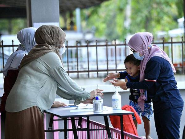 Pengasuh Taska Permata DD, Wan Nor Sazwanie Wan Mohd Nor (kiri) memberikan pensanitasi tangan kepada kanak-kanak Aidan Afham Ahmad Syahir (dua, kanan) ketika hadir di Taska Permata DD hari ini.