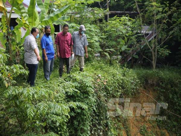 Syuhadak(kanan) menunjukkan masalah hakisan dan tanah runtuh di tebing Sungai Temiang di belakang rumahnya.