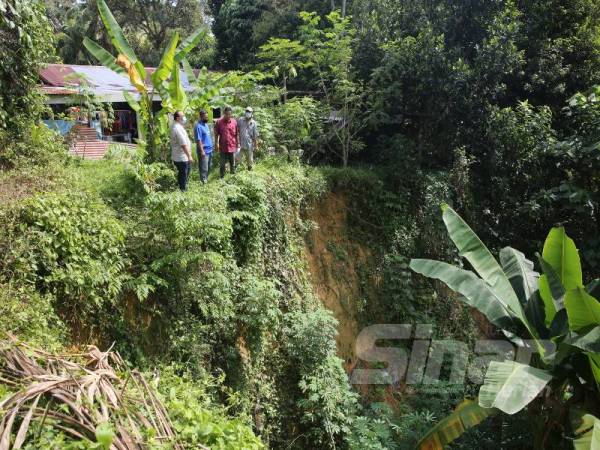 Syuhadak (kanan) menunjukkan masalah hakisan dan tanah runtuh di tebing Sungai Temiang di belakang rumahnya.