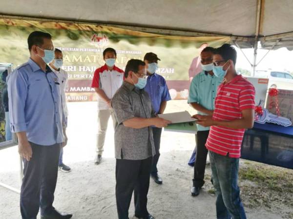 Ahmad (tengah) menyerahkan borang program Agropreneur Muda kepada Zakaria sempena lawatan beliau di Skim Padi Paya Mambang dekat Pekan kelmarin.