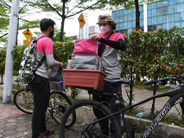 Rakan Penghantar Makanan Muqriz Rahman (kanan) dan Mak Sai Kam memasukkan makanan sebelum menghantar pesanan tersebut kepada pelanggan ketika tinjauan di sekitar ibu kota hari ini.