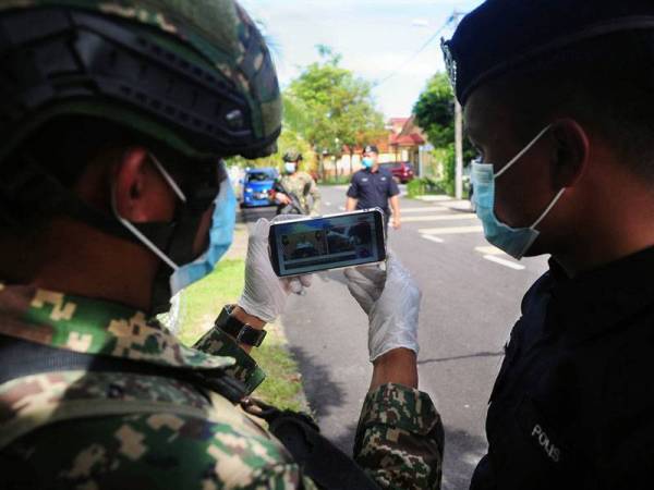 Anggota Polis dan Angkatan Tentera Malaysia melihat Perutusan Khas Perdana Menteri melalui telefon bimbit semasa waktu rehat ketika tinjauan hari kelima Perintah Kawalan Pergerakan secara pentadbiran di Taman Langat Utama Kuala Langat hari ini.