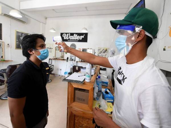 Saiful Anuar Musa (kanan) memeriksa suhu badan pelanggan Ahmad Haziq Ridzwan yang hendak memotong rambut di kedainya. - Foto Bernama