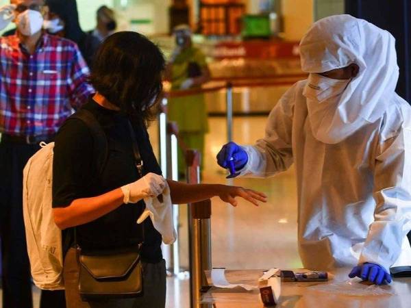 Seorang pekerja kesihatan memakai peralatan perlindungan diri (kanan) mengecop tangan seorang penumpang yang baru tiba di Lapangan Terbang Antarabangsa Chhatrapati Shivaji Maharaj, India baru-baru ini. - Foto AFP 