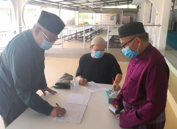 Noh (kiri) memeriksa suhu dan mendaftar bagi menunaikan solat Jumaat di Masjid Ar-Raudhah Tanjong Karang di sini hari ini.