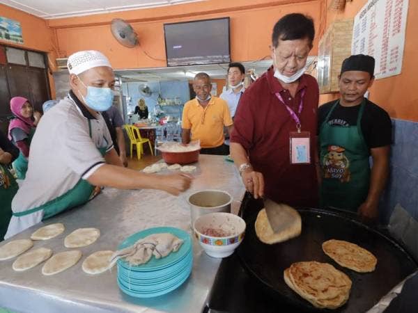 Tengku Zainul Hisham (tengah) cuba memasak roti canai pada sesi turun padang bertemu rakyat pagi tadi.