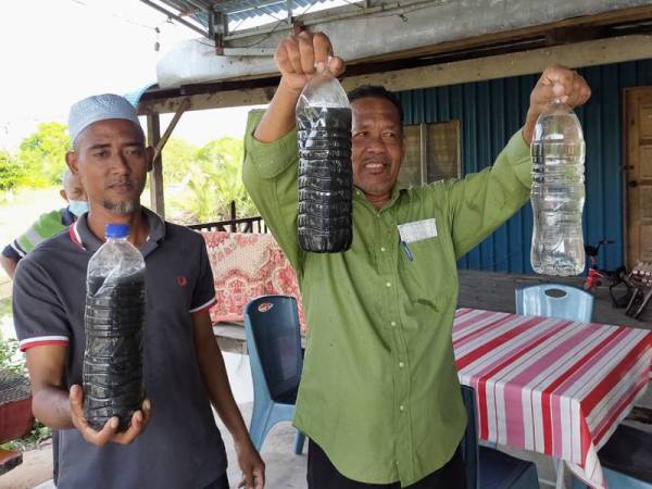 Rudi (kiri) dan Che Ani menunjukkan perbezaan warna air sungai Kuala Kerpan yang tercemar.