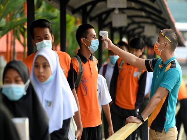 Seorang guru mengambil bacaan suhu badan pelajar sebelum memasuki sekolah di Sekolah Menengah Kebangsaan Elopura hari ini. Foto Bernama 