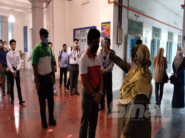 Guru mengambil bacaan suhu pelajar sebelum masuk ke kelas. 