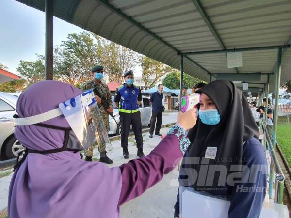 Salah seorang pelajar sedang melakukan saringan suhu sebelum dibenarkan masuk ke dalam kawasan sekolah.