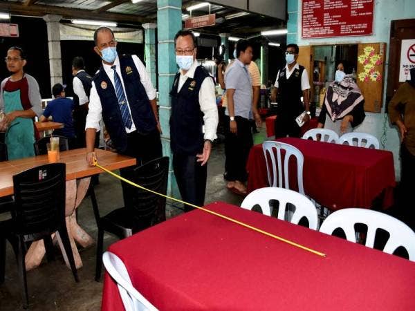 Anggota Jabatan Kesihatan Melaka, Zulbahri Zakaria (dua, kiri) melakukan pengukuran jarak meja pada salah sebuah premis makanan bagi memastikan para peniaga mematuhi prosedur operasi standard yang ditetapkan. - Foto Bernama