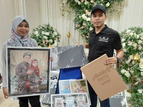 Faris (kanan) menyerahkan tempahan gambar perkahwinan kepada salah seorang pelanggannya.